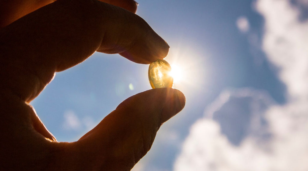 Hand holding a vitamin D supplement capsule in front of the sun.