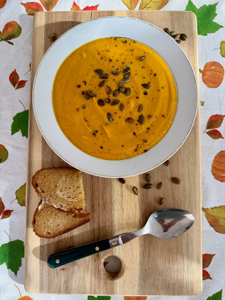 Creamy roasted red kuri squash and coconut soup topped with toasted pumpkin seeds, served with gluten-free sourdough bread.